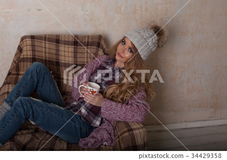 a girl sits in a chair with cup of coffee or tea 34429358