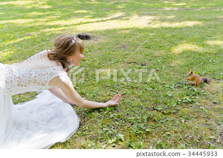 Bride in white lying on grass next to the squirrel 34445933