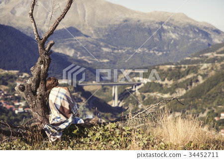 A girl wrapped up in a plaid sitting on a tree A girl wrapped up in a plaid sitting on a tree 34452711