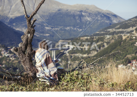 A girl wrapped up in a plaid sitting on a tree A girl wrapped up in a plaid sitting on a tree 34452713