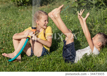 Happy kids sitting on the grass and pouring water from a hose. Happy kids sitting on the grass and pouring water from a hose. 34473935