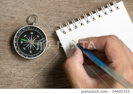 Man hold pen to write on note book with compass Man hold pen to write on note book with compass 34485355