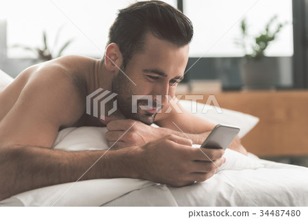 Joyful guy messaging on mobile phone in bedroom 34487480