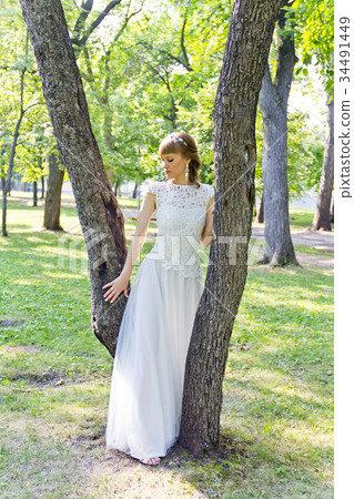 Bride in white lace dress standing near tree Bride in white lace dress standing near tree 34491449
