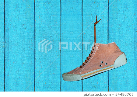 Single Trendy Gym shoe hangs on blue wooden wall. Single Trendy Gym shoe hangs on blue wooden wall. 34493705