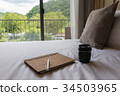 a camera lens, a pen and a notebook on the bed 34503965