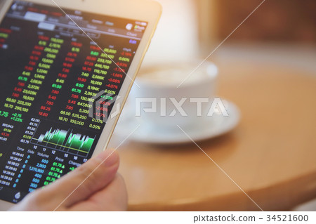 Business Hand Analyzing Stock finance Graph on Tablet with Coffee on wood background Business Hand Analyzing Stock finance Graph on Tablet with Coffee on wood background 34521600