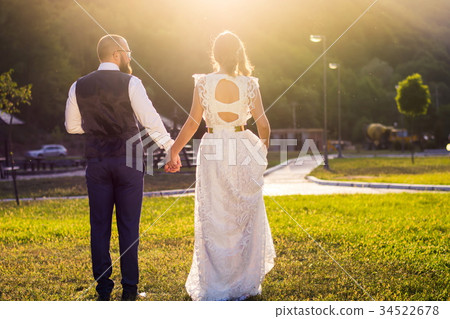 Bride and groom walking towards sunset holding hands Bride and groom walking towards sunset holding hands 34522678