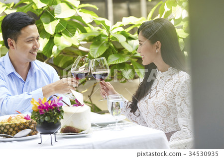 A couple is clinking wine glasses with happy smiles on their faces 34530935