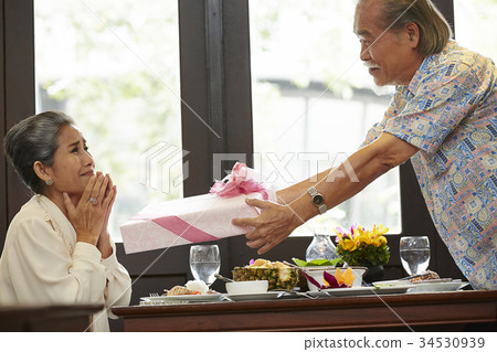 a senior couple is happily dating at a restaurant with a gift pink box a senior couple is happily dating at a restaurant with a gift pink box 34530939