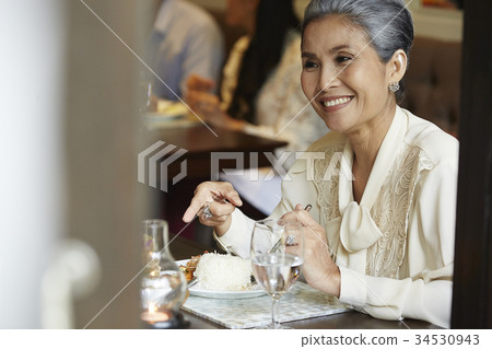 The older woman is smiling and pointing at foods on a table in a restaurant The older woman is smiling and pointing at foods on a table in a restaurant 34530943