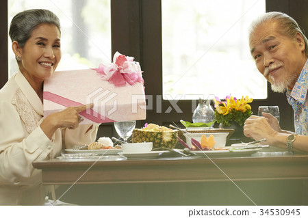 a senior woman is pointing a gift box while sitting in a restaurant with her husband a senior woman is pointing a gift box while sitting in a restaurant with her husband 34530945
