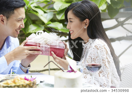 a happy young couple is holding a gift box when having lunch in restaurant 34530998