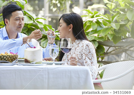An Asian man is feeding his girlfriend at a meal in a restaurant. An Asian man is feeding his girlfriend at a meal in a restaurant. 34531069