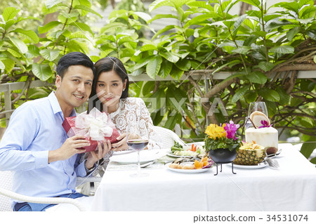An Asian couple is holding a gift when dating at a restaurant. 34531074