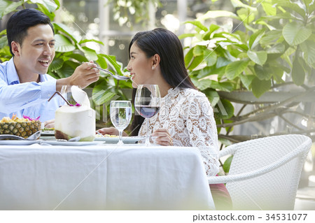 A young woman is feeling happy when her boyfriend feeds her at a restaurant. A young woman is feeling happy when her boyfriend feeds her at a restaurant. 34531077