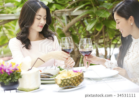 Two young women are smiling and holding wine glasses in a restaurant. 34531111