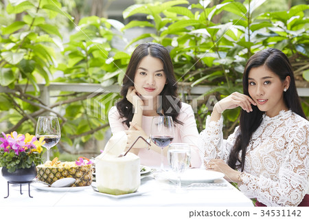 two women are sitting beside a banquet table and looking something 34531142