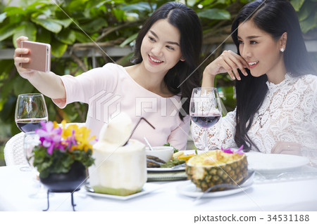 two beautiful ladies are taking selfie together in the banquet outdoors 34531188