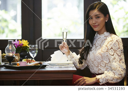 an attractive woman is holding wine glass in hand and smiling in a restaurant an attractive woman is holding wine glass in hand and smiling in a restaurant 34531193