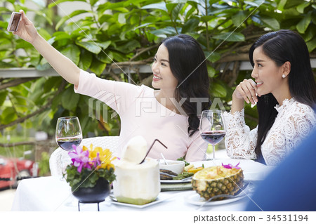 a lovely girl and friend are looking at her phone, smiling and taking selfie 34531194