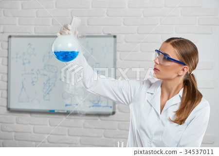 Young woman analyzes the blue chemical liquid Young woman analyzes the blue chemical liquid 34537011
