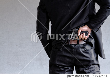 Man in business suit hiding gun behind his back 34537451