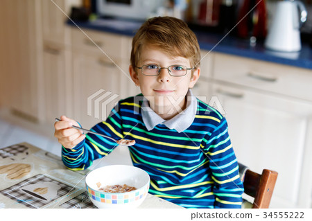 Happy little blond kid boy eating cereals for 34555222