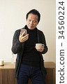 60s man operating a smartphone with a cup 34560224
