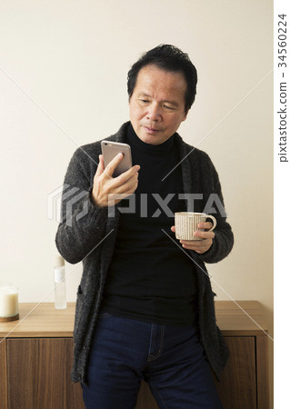 60s man operating a smartphone with a cup 60s man operating a smartphone with a cup 34560224
