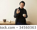 60s man operating a smartphone with a cup 34560363