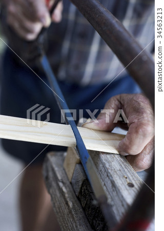 old man sawing a wood strip with a hand saw old man sawing a wood strip with a hand saw 34563213