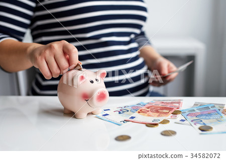 Pregnant woman putting coin into piggy bank 34582072