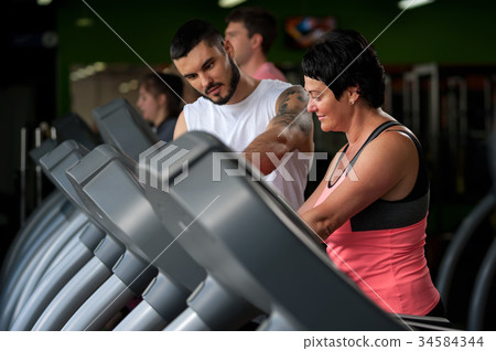 Fitness coach assisting his client on treadmill 34584344