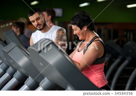 Fitness coach assisting his client on treadmill 34584356