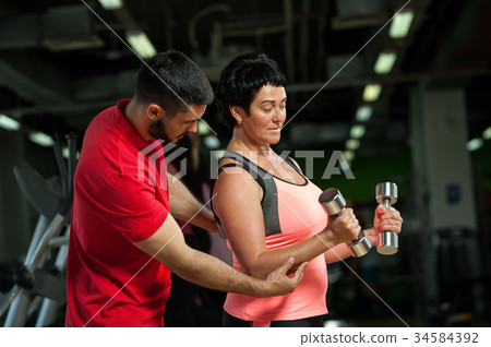 Personal coach with middle aged female in gym 34584392