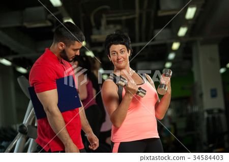 Middle aged woman working out with coach in gym Middle aged woman working out with coach in gym 34584403
