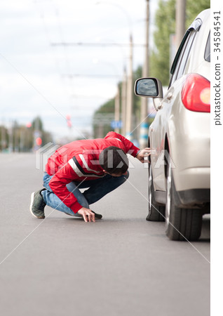 Young driver checking wheel after car breakdown. 34584541