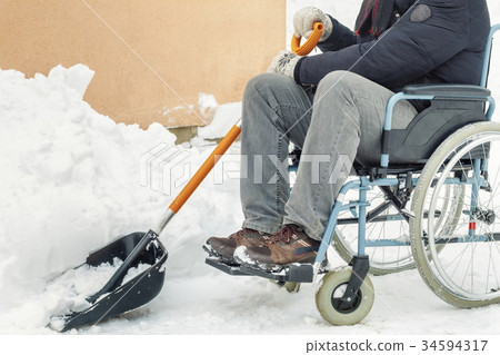 Disabled man on wheelchair with snow showel in the Disabled man on wheelchair with snow showel in the 34594317