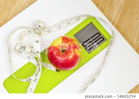 Apple with measuring tape close up on digital scal 34603254