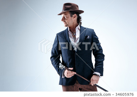The mature man in a suit and hat holding cane. 34605976