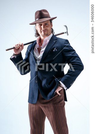 The mature man in a suit and hat holding cane. 34606000