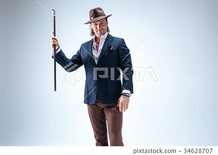 The mature man in a suit and hat holding cane. 34628707