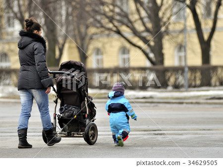 Mother with stroller walking near little son Mother with stroller walking near little son 34629505