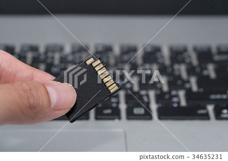 hand holds SD card with laptop background hand holds SD card with laptop background 34635231