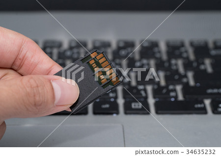 hand holds SD card  with laptop background 34635232