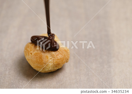 pouring dark chocolate on profiterole on parchment pouring dark chocolate on profiterole on parchment 34635234