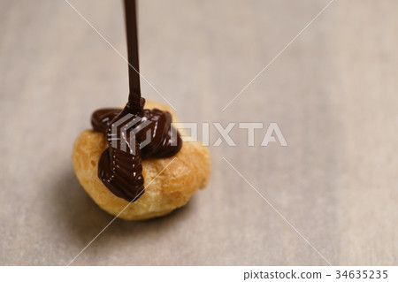pouring dark chocolate on profiterole on parchment 34635235