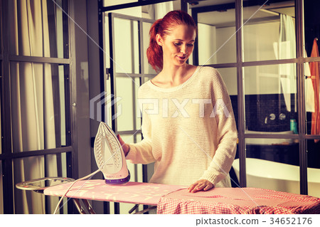 Red-haired young beautiful woman ironing clothes 34652176