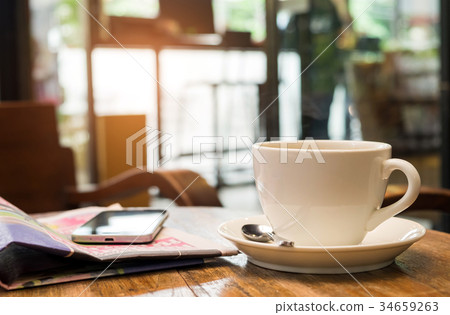 Coffee and a smart phone are on the newspaper. Coffee and a smart phone are on the newspaper. 34659263
